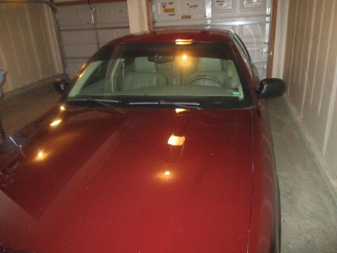 2004 Ford Crown Victoria - The front view of a dark red sedan parked in a garage. The car's hood and windshield are visible, reflecting overhead lights.
