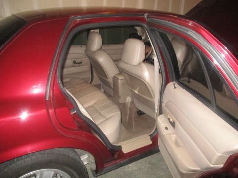 2004 Ford Crown Victoria - The interior of a red 2004 Ford Crown Victoria is shown with the rear passenger door open. The tan leather seats and door panel are visible.