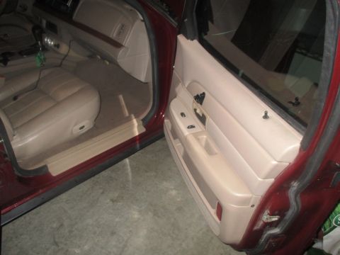 2004 Ford Crown Victoria - The interior of a maroon sedan is shown with the driver's side door open. The tan leather seat and door panel are visible, along with the d…