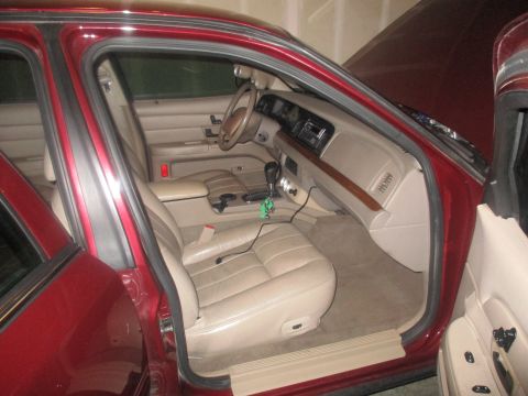 2004 Ford Crown Victoria - Interior view of a red sedan, likely a Ford Crown Victoria, showing the driver's side front seat, dashboard, and center console. The car's…
