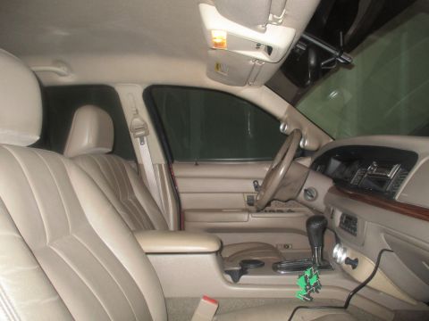 2004 Ford Crown Victoria - The interior of a sedan shows tan leather seats, a tan dashboard with wood trim accents, and a center console with a gear shifter. A black…