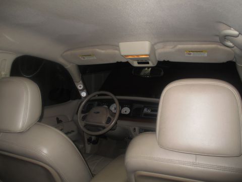 2004 Ford Crown Victoria - The interior of a car is shown from the back seat, looking towards the front. The view includes tan leather seats, the steering wheel, dash…