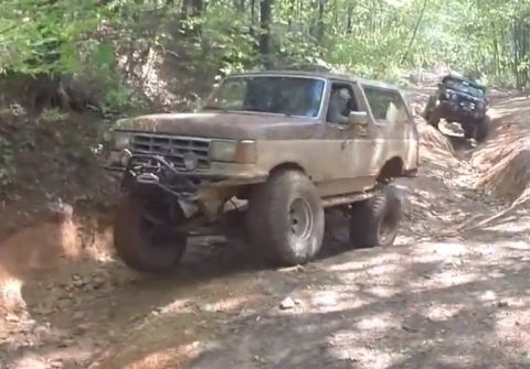 1988 Ford Bronco - A heavily modified, lifted 1988 Ford Bronco is navigating a steep, muddy off-road trail with another off-road vehicle visible further up th…