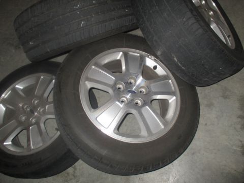 2004 Ford Crown Victoria - Four tires and alloy wheels are stacked on a concrete floor. Three of the wheels are visible, showing a silver five-spoke design with a blu…