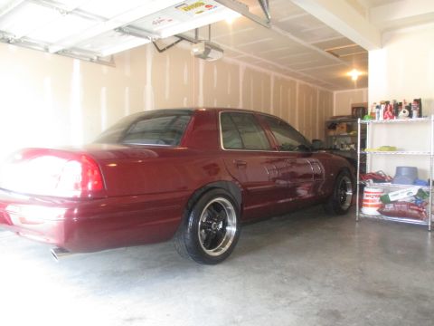 2004 Ford Crown Victoria - A maroon Ford Crown Victoria is parked in a garage. The car is viewed from the rear quarter angle, showing its custom wheels and exhaust pi…