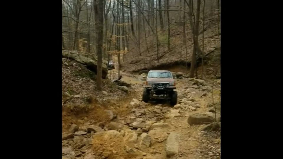 Brown Ford Bronco off-roading on a rocky, wooded trail.