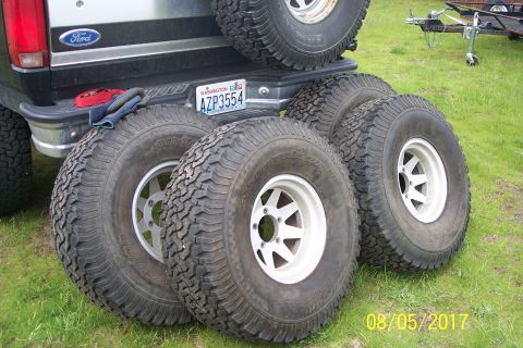 1989 Ford Bronco - Four off-road tires with white rims are laid out on the grass next to the rear of a Ford pickup truck. A Washington license plate is visibl…