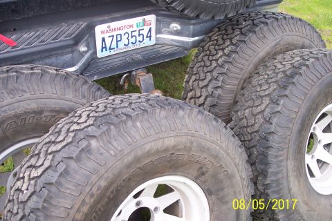 1989 Ford Bronco - A Washington state license plate reading AZP3554 is mounted on the tailgate of a dark-colored pickup truck, with four off-road tires stacke…