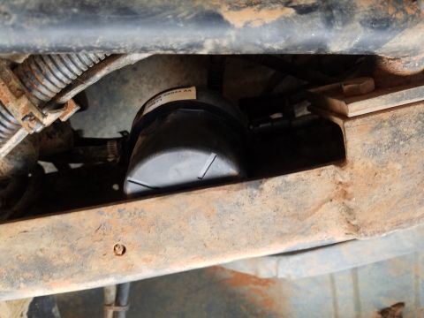 1988 Ford Bronco - A black fuel filter is visible, mounted to the underside of a rusty vehicle frame. A white label with black text is affixed to the fuel fil…