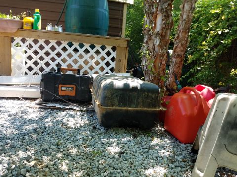 1988 Ford Bronco - A collection of outdoor items including a black toolbox, a large black container, and several red and orange gas cans are arranged on a gra…