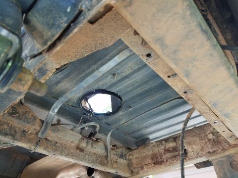 1988 Ford Bronco - The underside of a vehicle chassis shows significant rust on the frame and bed support beams, with a circular opening cut into the ribbed m…