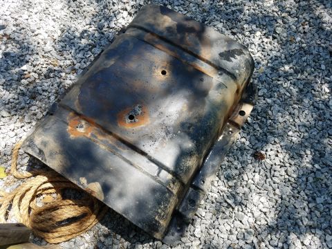 1988 Ford Bronco - A heavily rusted and dented black metal part, possibly a fuel tank, lies on a bed of gray gravel. A thick rope is coiled to the left of the…