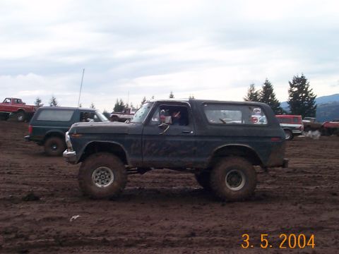 1983 Ford Bronco - A dark blue Ford Bronco is seen in a muddy field with other vehicles in the background.
