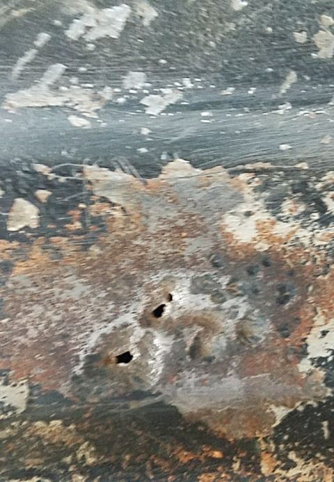 1988 Ford Bronco - Close-up view of rusted metal with two distinct holes, likely a vehicle part undergoing restoration or showing wear.
