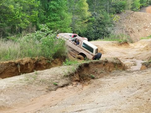 1988 Ford Bronco - A tan Ford Bronco is navigating a muddy, rutted off-road trail, with its front wheels tilted precariously.
