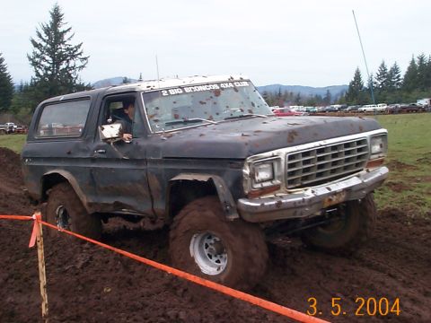1983 Ford Bronco - A black 1983 Ford Bronco navigates a muddy course, displaying a "2 BIG BRONCOS 4X4 CLUB" sticker on its windshield.