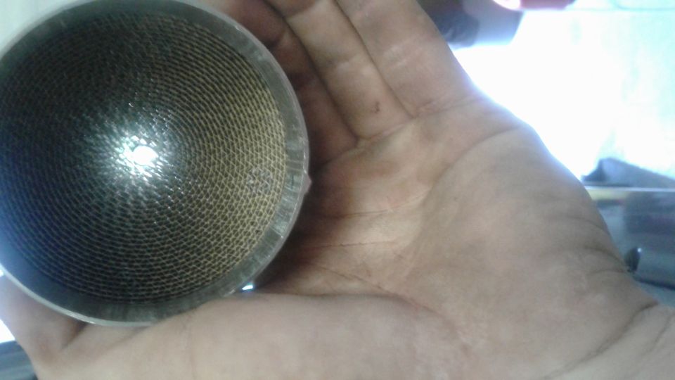 Close-up of a catalytic converter core held in a hand, showing honeycomb structure.