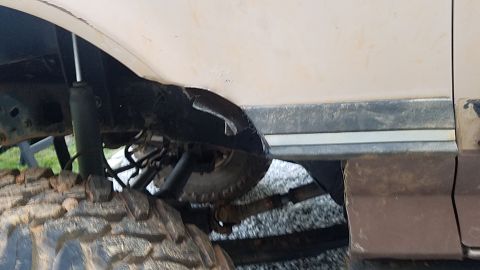 1988 Ford Bronco - A close-up view of the heavily modified suspension and fender area of a lifted vehicle, showing a large, aggressive tire and a damaged fend…