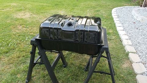 1988 Ford Bronco - A glossy black fuel tank sits on a black sawhorse stand outdoors on a grassy lawn. The tank has a ribbed top surface and an opening in the…