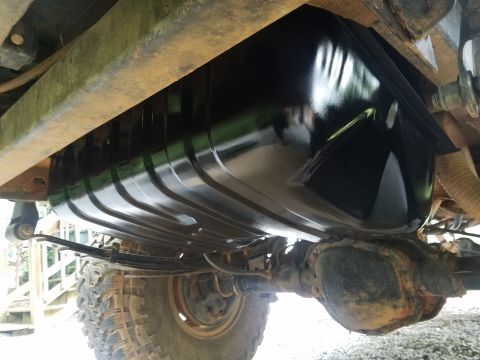 1988 Ford Bronco - The underside of a vehicle shows a new, glossy black fuel tank mounted above the rear axle and leaf springs. The vehicle's frame rails are…