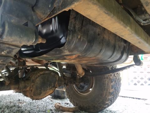 1988 Ford Bronco - The underside of a vehicle shows a large, black fuel tank mounted above the rear axle and leaf spring suspension. The vehicle appears to be…