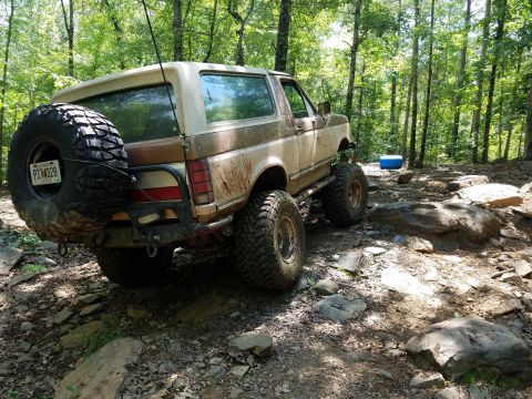 1988 Ford Bronco - This modified SUV navigates a challenging, rocky path through a dense forest environment.
