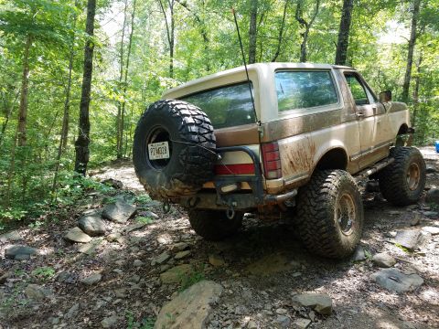 1988 Ford Bronco - This lifted Ford Bronco navigates a challenging rocky trail through a wooded area.