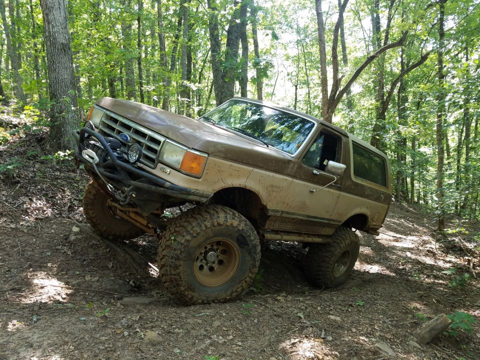 Brown Ford Bronco with off-road modifications on a dirt trail