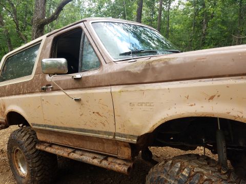 1988 Ford Bronco - This lifted 1988 Ford Bronco is covered in mud, suggesting recent off-road use.