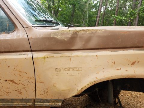 1988 Ford Bronco - A mud-covered Ford Bronco shows significant damage to its hood and fender.