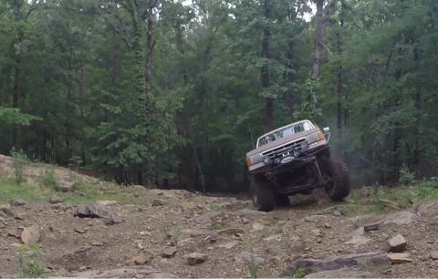 1988 Ford Bronco - This off-road SUV navigates a challenging rocky incline amidst a wooded area.
