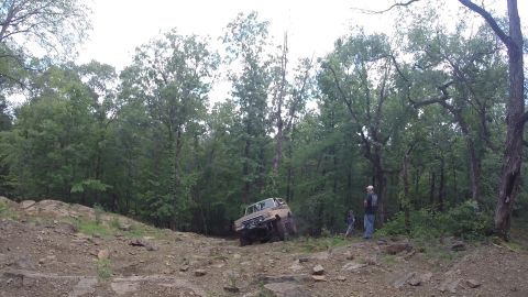 1988 Ford Bronco - An off-road vehicle navigates a challenging, rocky incline in a wooded area.