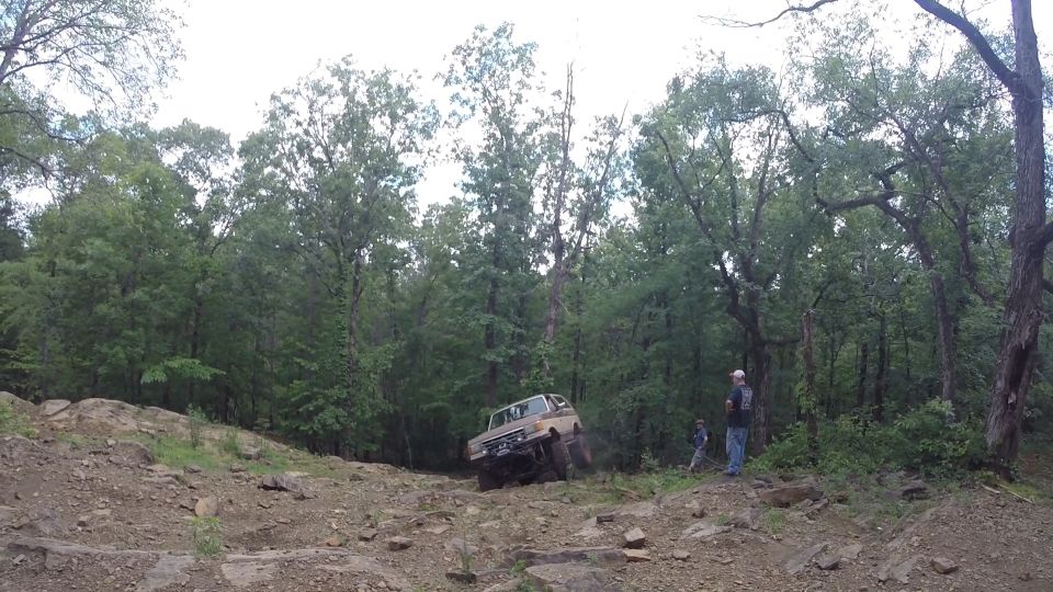 tan SUV climbing a steep, rocky trail with trees in the background