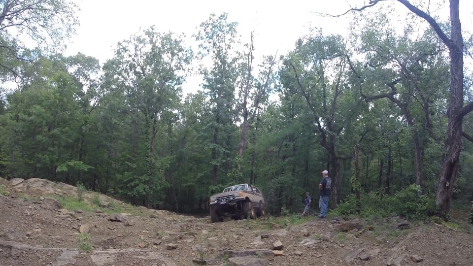 Tan Ford Bronco off-roading on a rocky trail with trees in the background