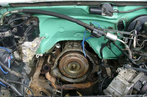 1992 Ford Bronco - Close-up view of the engine bay, focusing on the transmission and air conditioning components, with a teal-colored firewall.