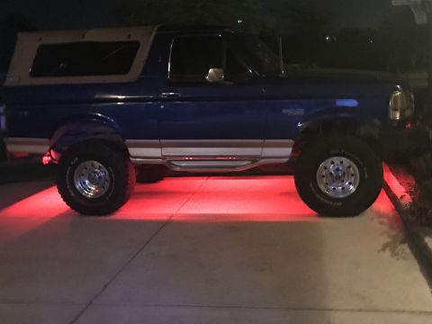 1996 Ford Bronco - Side view of a blue 1996 Ford Bronco with a tan soft top and custom red underglow lighting.
