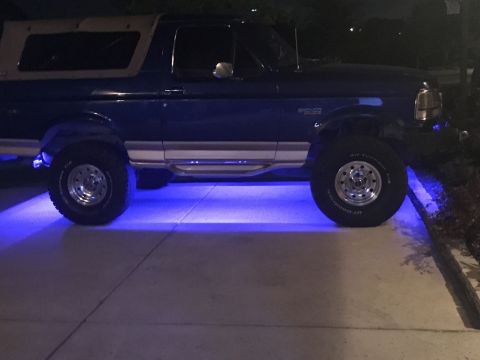 1996 Ford Bronco - A blue Ford Bronco with a tan top is parked at night, illuminated by blue underglow lights.