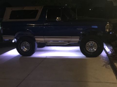 1996 Ford Bronco - A blue 1996 Ford Bronco with a tan top is parked at night, illuminated by underglow lights.