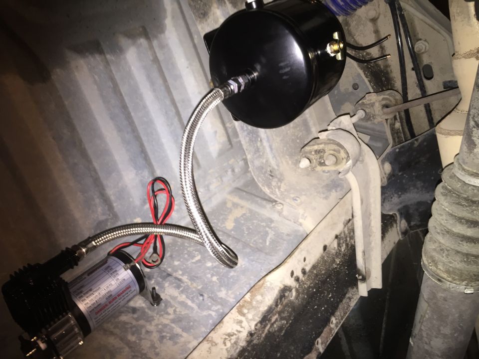 Under-vehicle air compressor and black tank with braided hoses. Some text visible on compressor label