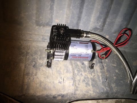 1996 Ford Bronco - An air compressor with a metal braided hose and red/black wires is attached to a textured surface.