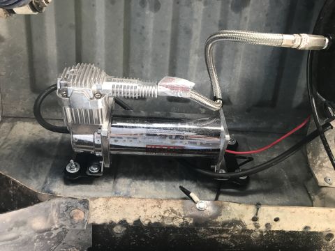 1996 Ford Bronco - A chrome air compressor with a silver braided hose is mounted in the bed of a vehicle.