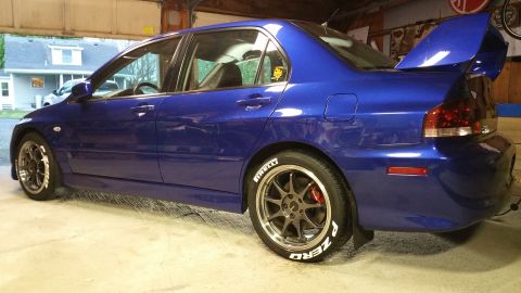 2006 Mitsubishi Evolution - A blue 2006 Mitsubishi Evolution sedan is parked in a garage, showing its distinctive rear spoiler and performance wheels.