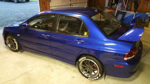 2006 Mitsubishi Evolution - A blue 2006 Mitsubishi Lancer Evolution VIII is parked in a garage, a prominent rear spoiler and custom wheels with white lettering on the…