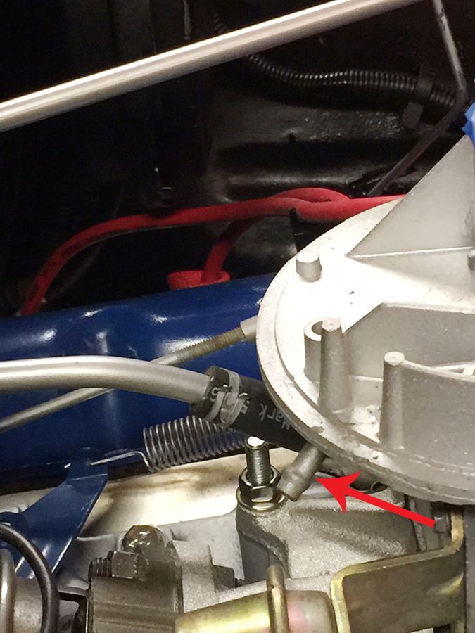 Close-up of a carburetor with a red arrow pointing to a vacuum line