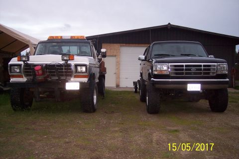 1995 Ford Bronco - Two Ford trucks are parked in front of a garage, one is a black Bronco and the other is a white truck.