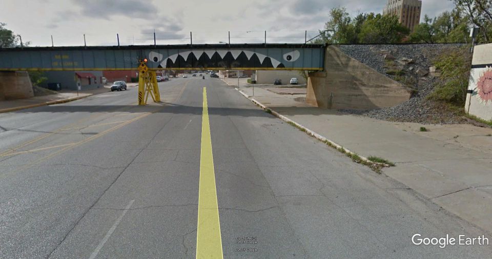 Road under a bridge painted with shark teeth, with cars visible in the distance