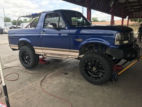 1996 Ford Bronco - A blue 1996 Ford Bronco is shown on jacks with aftermarket wheels and tires, possibly undergoing service.