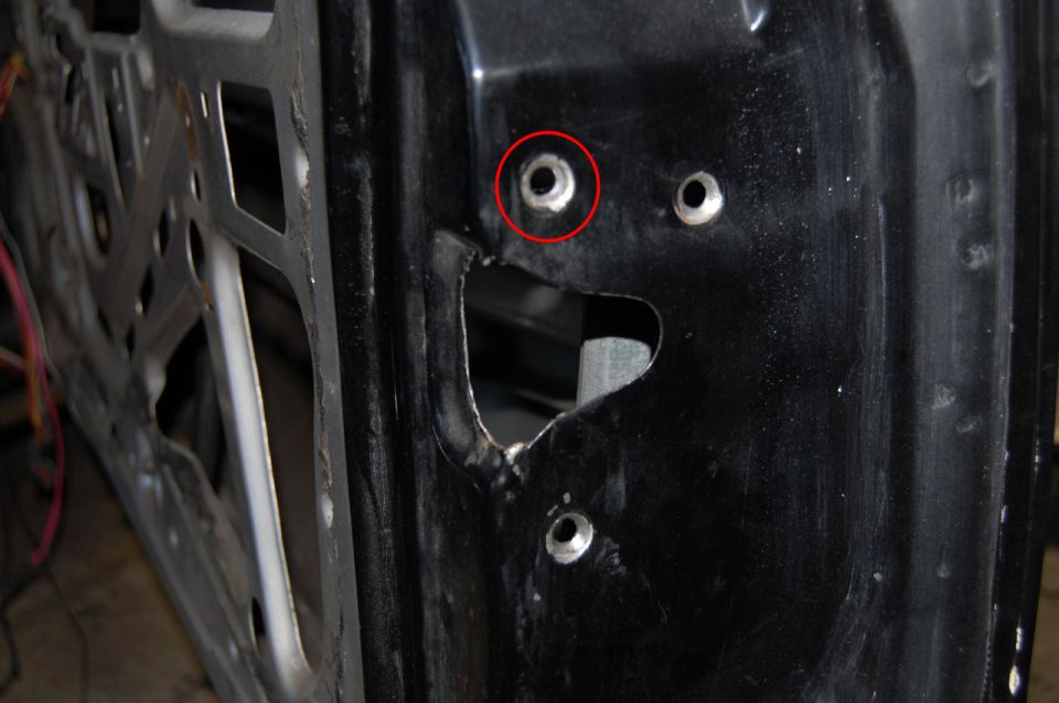 Close-up of a car door's inner structure with mounting holes. Red circle highlights one hole