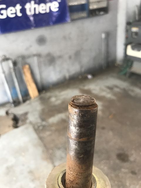 1996 Ford Bronco - A close-up shot focuses on a corroded metal pin, likely a component from a vehicle or machinery, in a workshop setting.