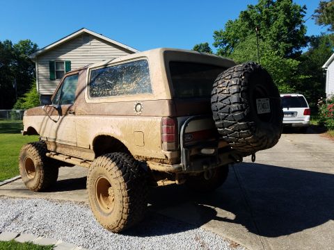 1988 Ford Bronco - This 1988 Ford Bronco is heavily covered in mud, showing its off-road capabilities. A spare tire is mounted on the rear, and a license plat…